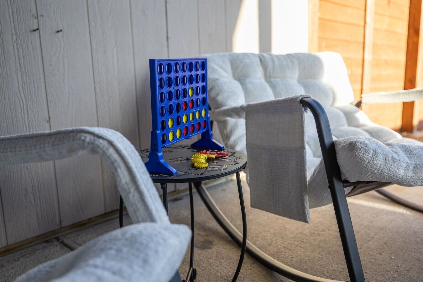 A blue game board with colorful pegs, a small round table, and two white cushioned chairs.