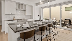 A modern kitchen with white cabinetry, a central island with bar stools, and a large sliding glass door leading to a balcony.