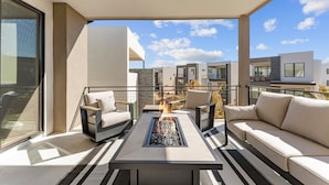 A modern balcony with a fire feature, seating, and a view of other buildings.