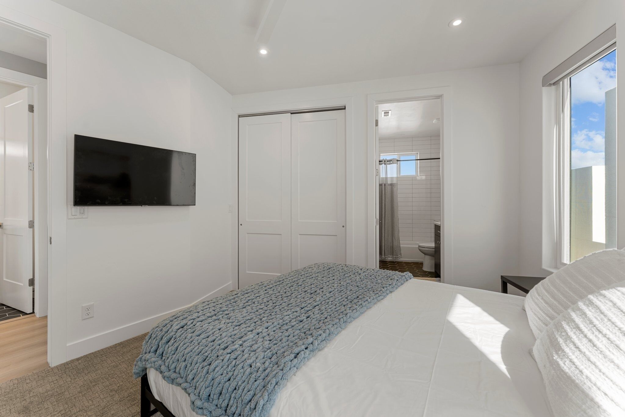 A bedroom with a bed, a TV mounted on the wall, a closet, and a bathroom visible through an open door.