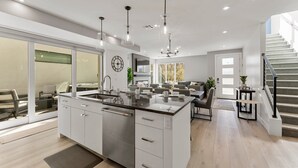Een moderne keuken met een groot eiland, ingebouwde apparatuur en hangende lampen.