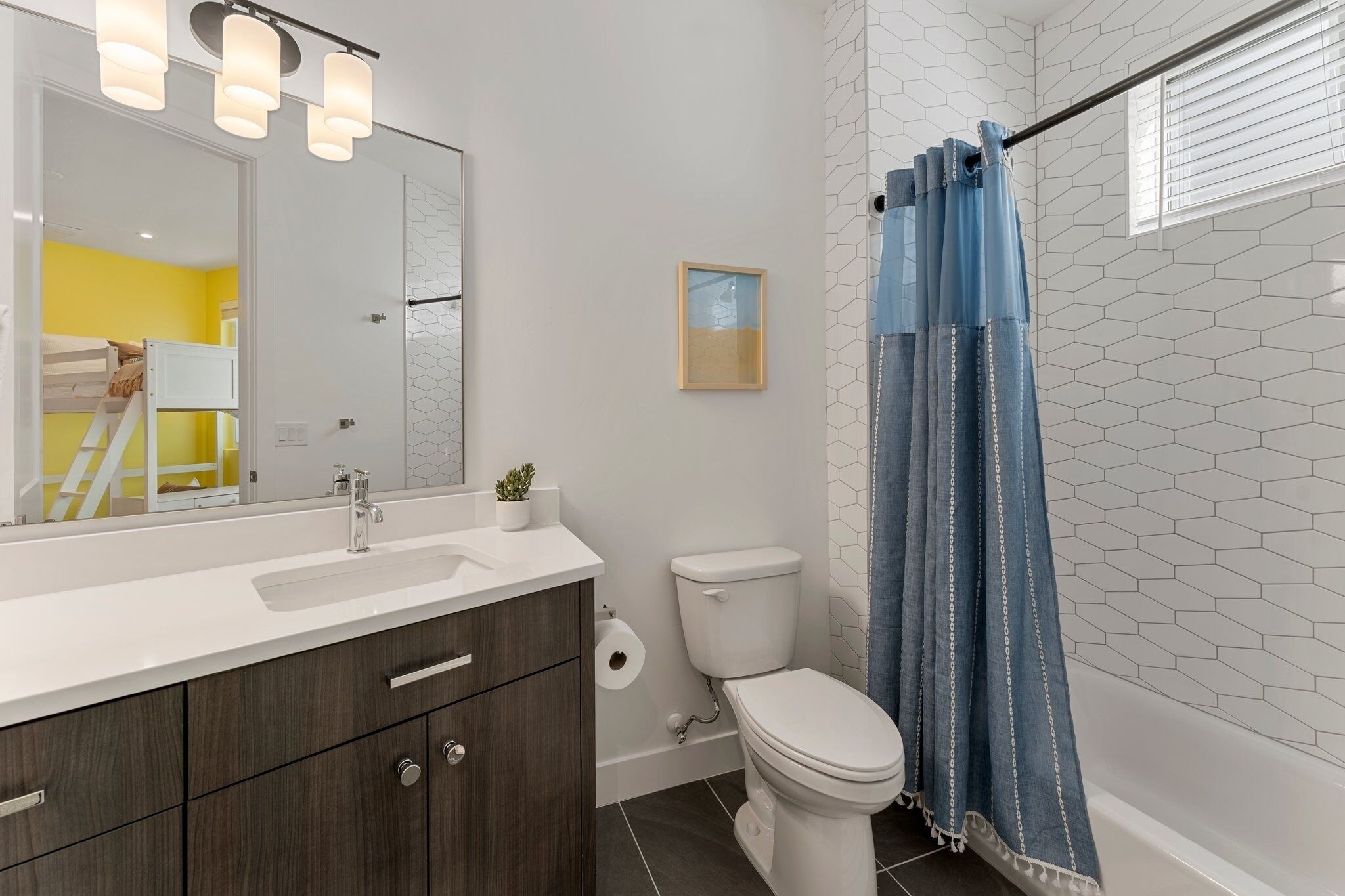 A modern bathroom with a white sink, dark wooden cabinets, a white toilet, and a shower with a blue curtain.