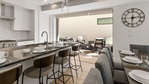 Een moderne keuken met een centraal eiland, barkrukken en een eethoek met een tafel voor vier personen.