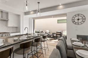 Een moderne keuken met een centraal eiland, barkrukken en een eethoek met een tafel voor vier personen.