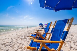 Une plage bordée de rangées de chaises de plage et de parasols bleus.