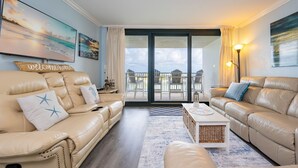 Una sala de estar con dos sofás de cuero color beige, una mesa de centro y un balcón con mobiliario de exterior.