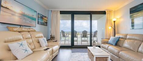 Un salon avec deux canapés en cuir beige, une table basse et un balcon aménagé avec du mobilier d’extérieur.