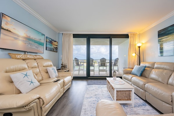 A living room with two beige leather sofas, a coffee table, and a balcony with outdoor furniture.