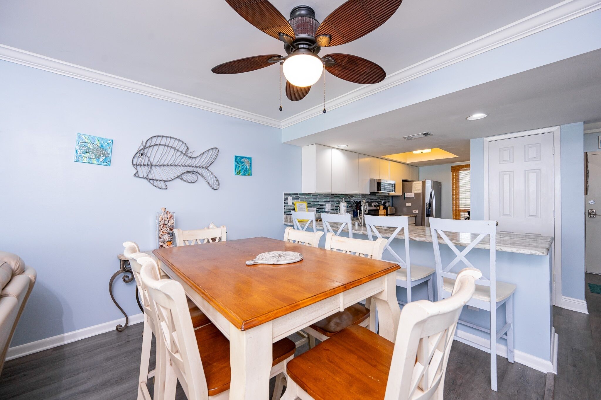 A dining area with a wooden table and white chairs, a ceiling fan, and artwork on the walls.