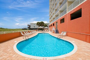 Una piscina amb gandules, una zona de seients coberta i un edifici amb balcons.