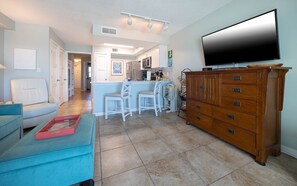 Una sala de estar moderna con un televisor de pantalla plana grande, un mueble de madera y una cocina al fondo.