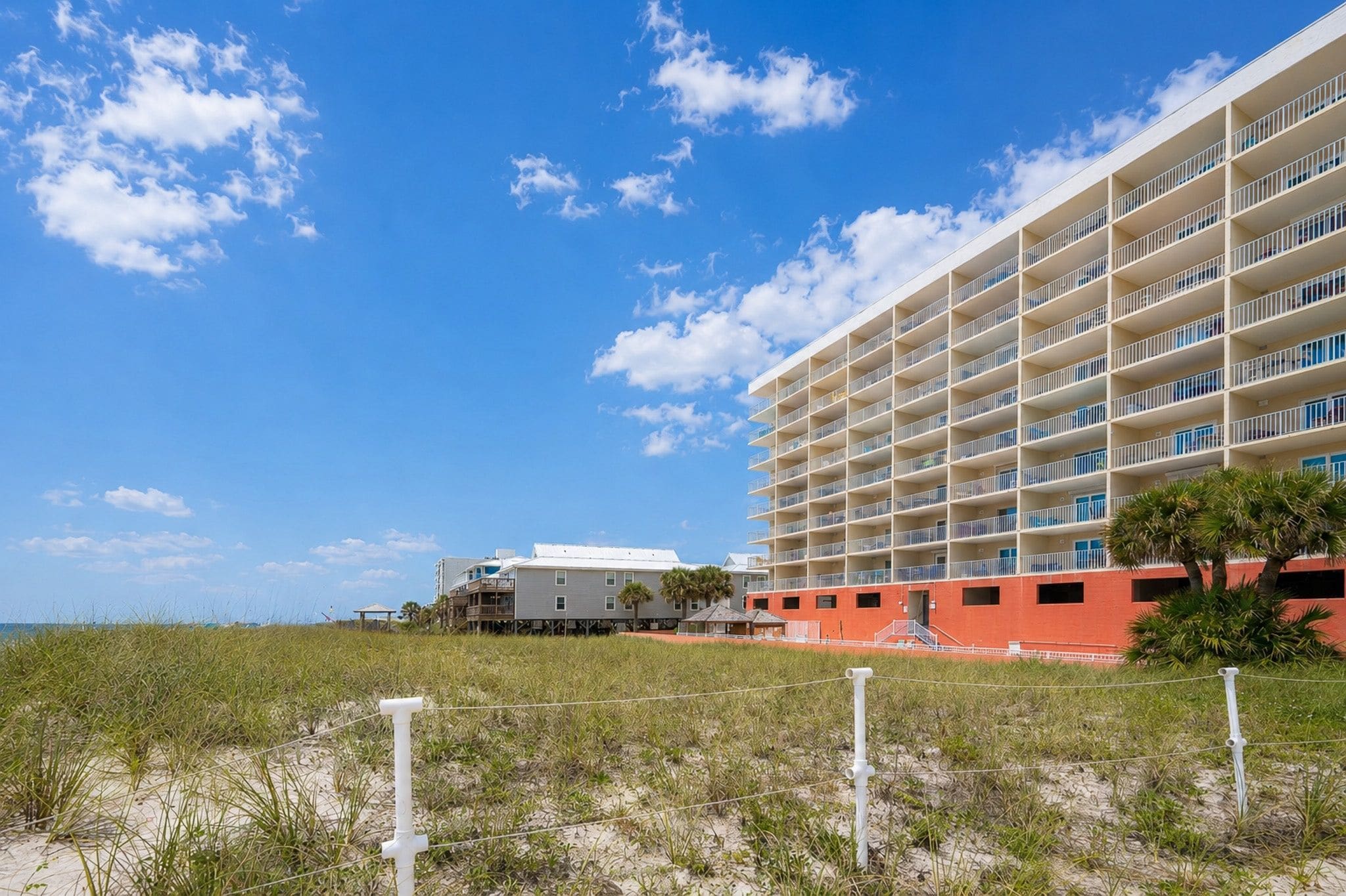 Un hôtel en bord de mer doté de nombreux balcons, une plage de sable en premier plan et un ciel bleu dégagé.