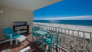 Ein Balkon mit Blick auf einen Strand, ein Stuhl, ein Tisch und ein Regal mit einem Schild, auf dem 'BEACH' steht.