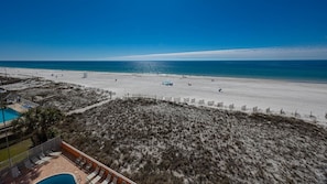 Blick auf einen Strand mit Poolbereich, einem eingezäunten Bereich und blauem Himmel.