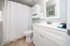 A bathroom with a toilet, a sink with a mirror, and a shower curtain. - Seacrest 506 1 Bedroom Condo (Gulf Shores)