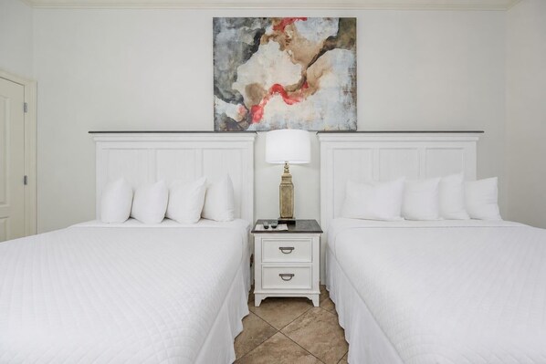 Habitación de hotel con dos camas, una mesita de noche con lámpara y un cuadro abstracto grande en la pared.