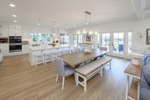 Una cocina amplia con armarios blancos, una isla grande y un comedor con una mesa de madera y bancos.