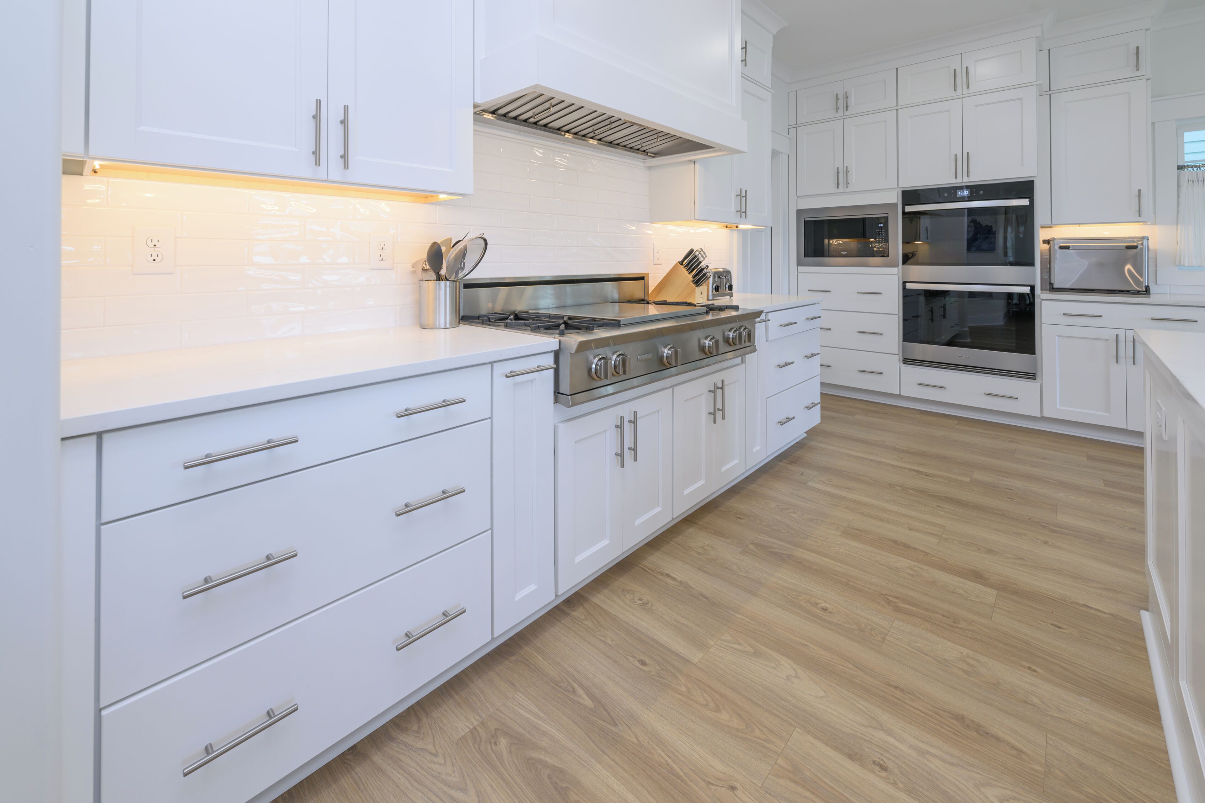 A modern kitchen with white cabinetry, a stainless steel stove, and wooden flooring.