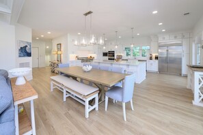 Une cuisine moderne avec des meubles blancs, un îlot central et un coin repas comprenant une table et un banc en bois.