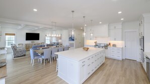Una cocina amplia con muebles blancos, una isla central e iluminación colgante.