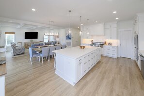 Une cuisine spacieuse avec des meubles blancs, un îlot central et des luminaires suspendus.