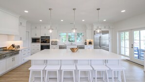 Una cocina amplia con armarios blancos, una isla grande con taburetes y electrodomésticos modernos.