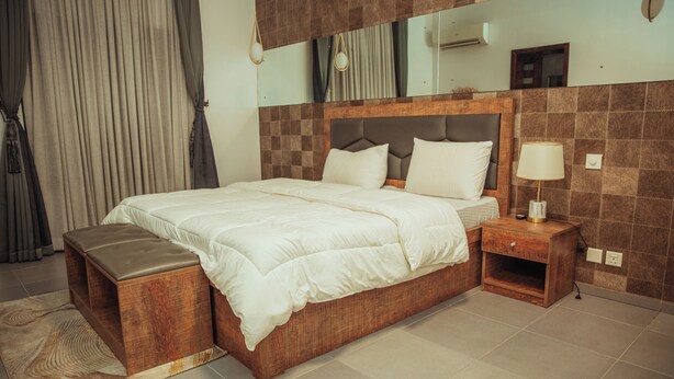 Een moderne hotelkamer met een groot bed, een houten hoofdeinde en een nachtkastje met een lamp.