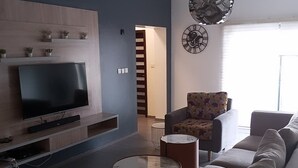 Een moderne woonkamer met een flatscreen televisie, een bank, een fauteuil met een patroon en een decoratieve klok.
