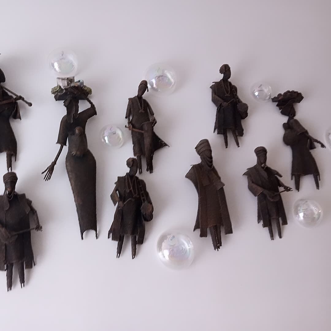 A collection of dark-colored, abstract figures with clear glass spheres, arranged on a plain surface.