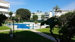 A pool area with a clear blue pool, surrounded by a fence, and a pathway leading to a building with multiple floors.