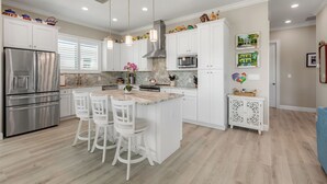 A modern kitchen with white cabinetry, stainless steel appliances, and a central island with bar stools. - ARTIST HOUSE ~ Canal Front 4 BR/3.5 Ba Home w/ Pool & Ocean and Gulf Access! (Cudjoe Key)