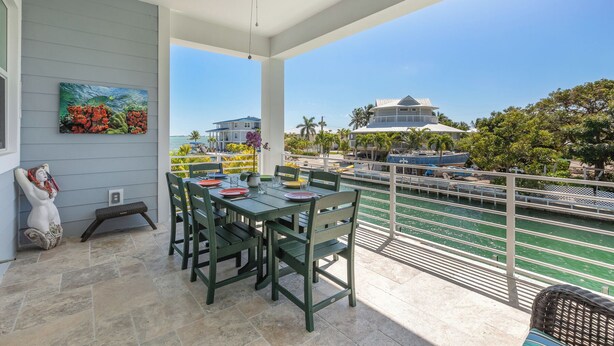 A covered outdoor dining area with a view of the sea and buildings. - ARTIST HOUSE ~ Canal Front 4 BR/3.5 Ba Home w/ Pool & Ocean and Gulf Access! (Cudjoe Key)