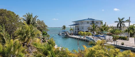 A waterfront property with a large house, docked boats, and lush tropical vegetation.