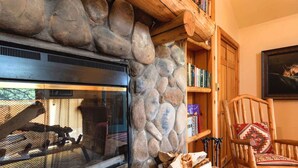 Una chimenea de piedra con puerta de vidrio, una estantería de madera y un sillón con cojín estampado.