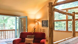 Una habitación acogedora con un sofá rojo, una viga de madera y un ventanal con vistas a árboles.