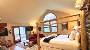 Una habitación acogedora con una cama nido de madera, una silla roja, una mesita y un gran ventanal con vistas a árboles.