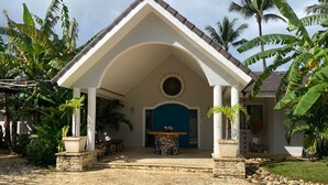 Un bâtiment à la façade blanche, avec une porte bleue et une entrée pavée de pierres.