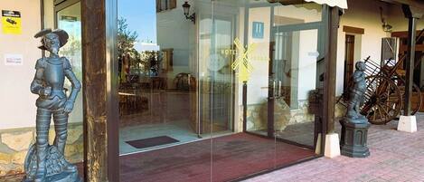 A hotel entrance with a glass door, a stone statue on the left, and a wooden cart on the right.