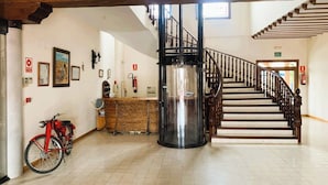 A spacious lobby with a wooden staircase, a reception desk, and a red bicycle. - Hotel A Posada (Tembleque)