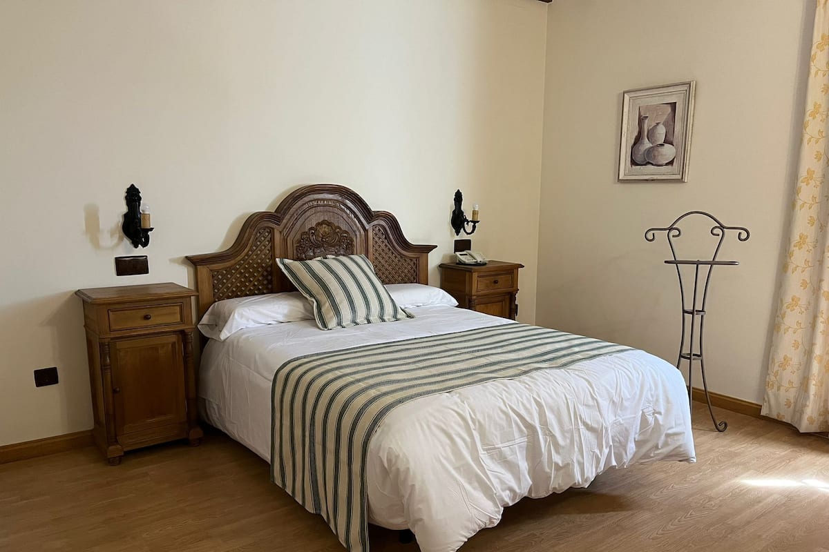 A neatly made bed with a striped bedspread, wooden nightstands with lamps, and a wall-mounted picture.