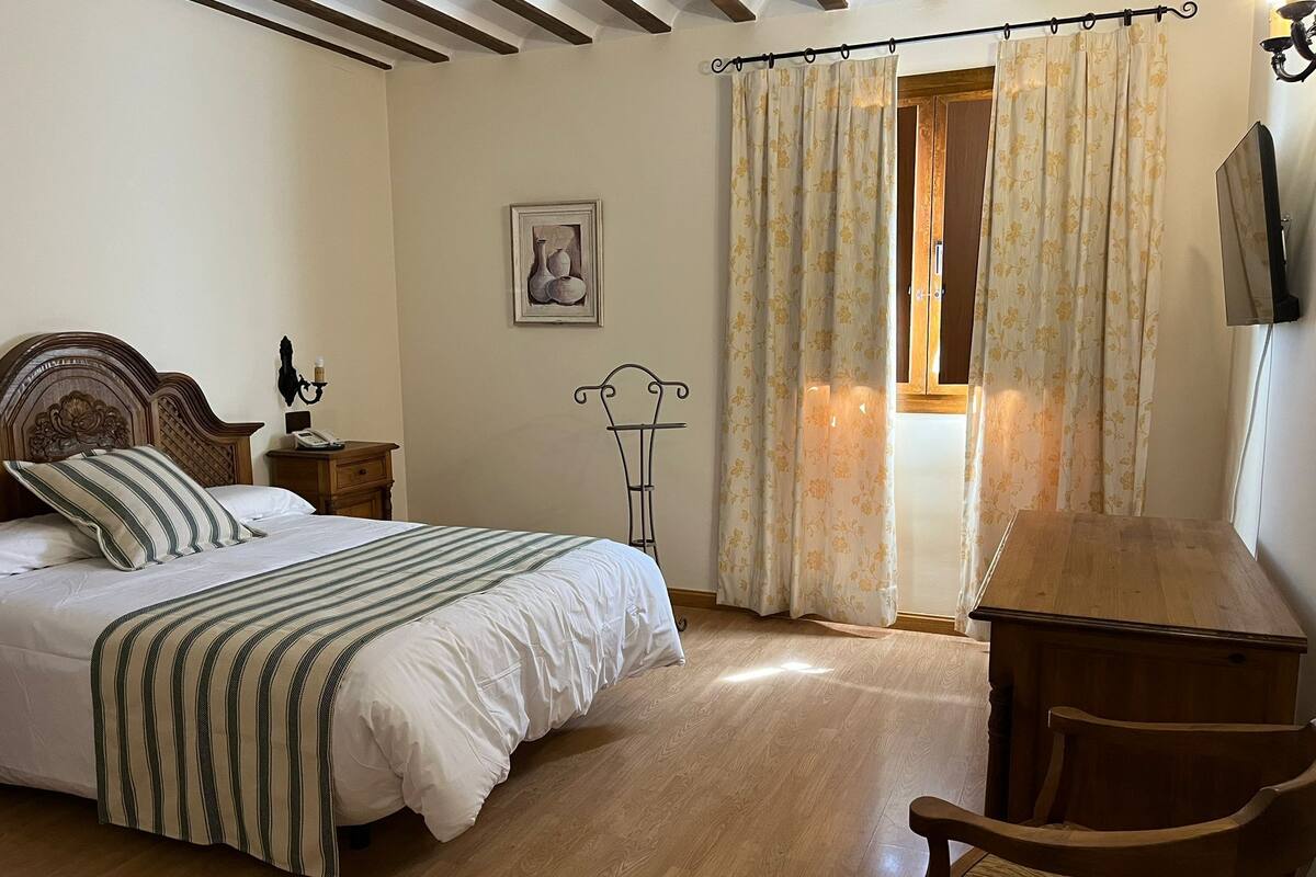 A bedroom with a wooden bed, a bedside table, a chair, and a window with curtains.