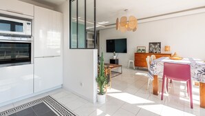 A modern kitchen with built-in appliances, a dining area with a table and chairs, and a living space with a flat-screen TV and decorative items.