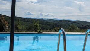 Una terraza de madera con piscina, un sombrero de paja y gafas de sol.