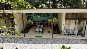 A modern outdoor kitchen area with a dining table and chairs, surrounded by greenery and a gravel path. - Casa Rio Tortuga - 2 Bedrooms with Outdoor Dining Area (Ojochal)