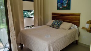 A neatly made bed with a wooden headboard, a butterfly painting on the wall, and a window with curtains. - Casa Rio Tortuga - 2 Bedrooms with Outdoor Dining Area (Ojochal)