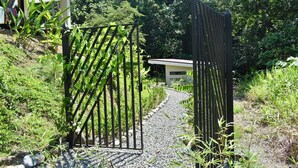 A pathway leading to a building with a black gate, surrounded by greenery and a gravel path. - Casa Rio Tortuga - 2 Bedrooms with Outdoor Dining Area (Ojochal)