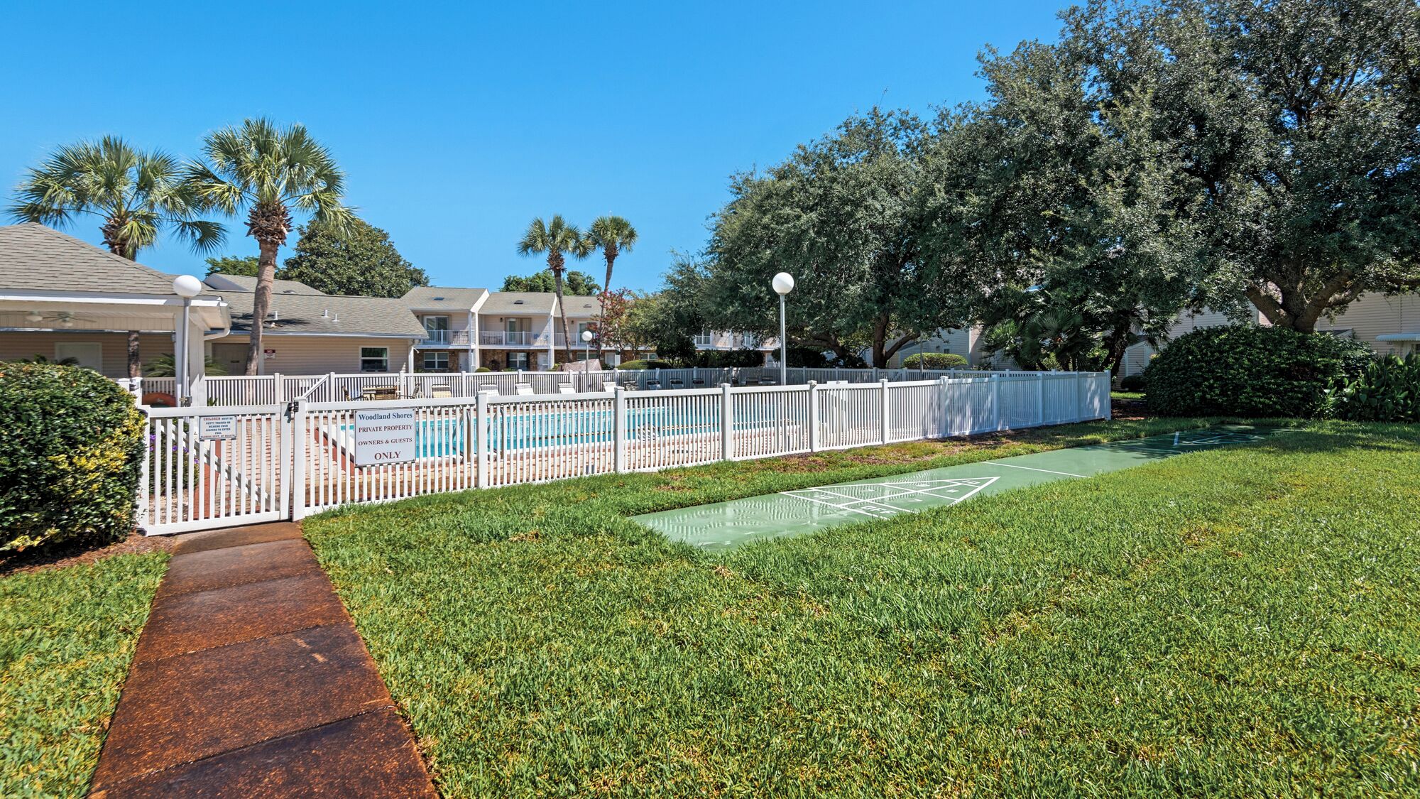 A fenced private property with a pool, a walking path, and a green lawn.
