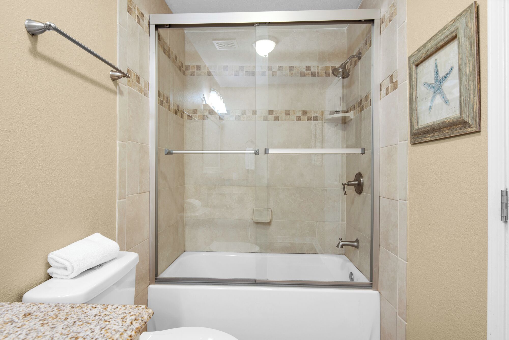 Eine Duschkabine mit Glas, eine weiße Badewanne und ein Handtuch auf der Toilette.