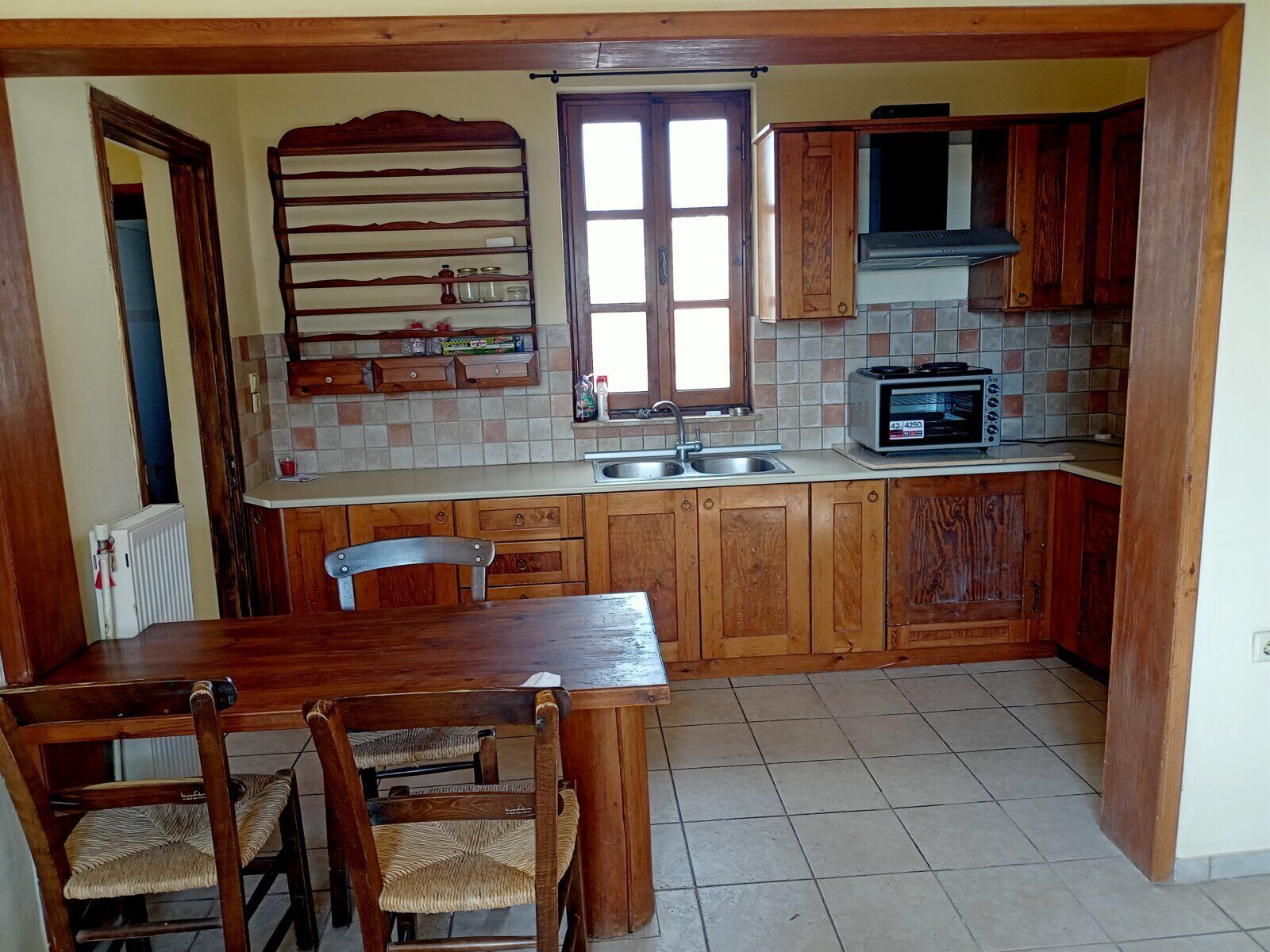 Una cocina con armarios de madera, salpicadero de azulejos, horno empotrado y una zona de comedor con mesa y sillas.