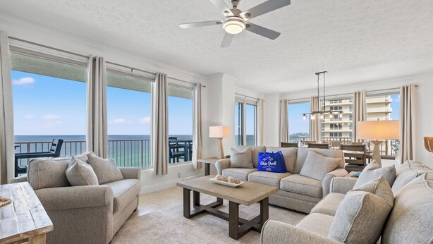 A spacious living room with a large window overlooking the ocean, a ceiling fan, and a seating area with a coffee table.
